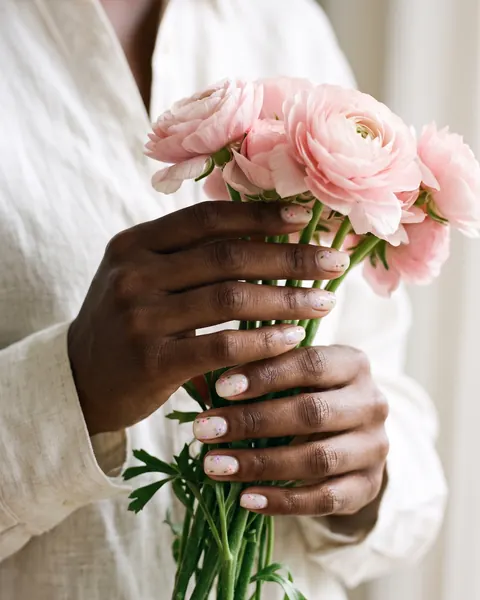 Short nails with tiny hand-painted pastel flowers holding pink ranunculus